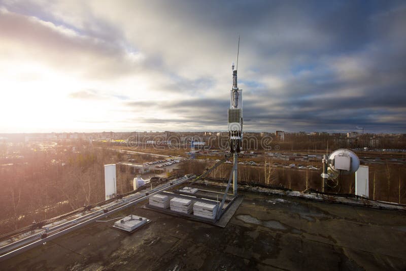 Panel antenna of GSM DCS UMTS LTE bands and radio unit are as part of communication equipment of basic station are installed on the roof and sky and city are as background. Panel antenna of GSM DCS UMTS LTE bands and radio unit are as part of communication equipment of basic station are installed on the roof and sky and city are as background