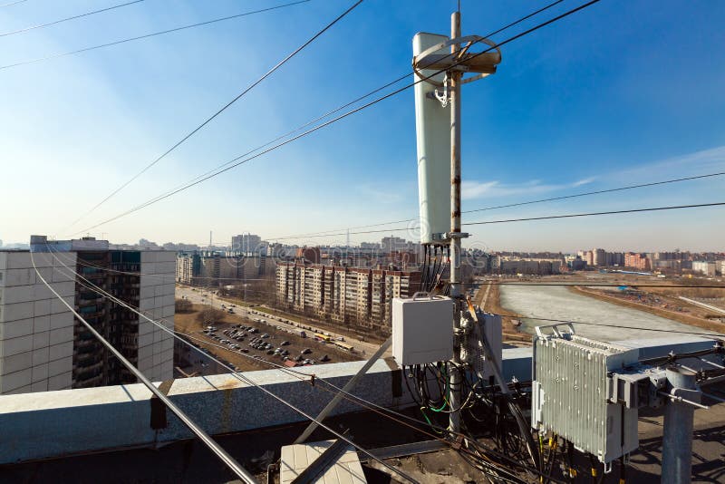 Panel antenna of GSM DCS UMTS LTE bands and radio unit are as part of communication equipment of basic station are installed on the roof and sky and city are as background. Panel antenna of GSM DCS UMTS LTE bands and radio unit are as part of communication equipment of basic station are installed on the roof and sky and city are as background.