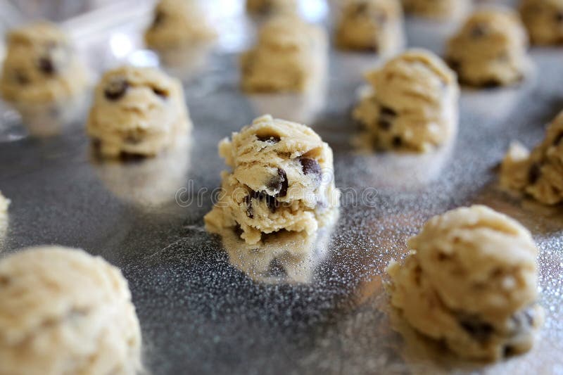 A tray lined with aluminum foil and greased is full of homemade chocolate chip cookies rolled from fresh dough and about to be baked in the oven. A tray lined with aluminum foil and greased is full of homemade chocolate chip cookies rolled from fresh dough and about to be baked in the oven