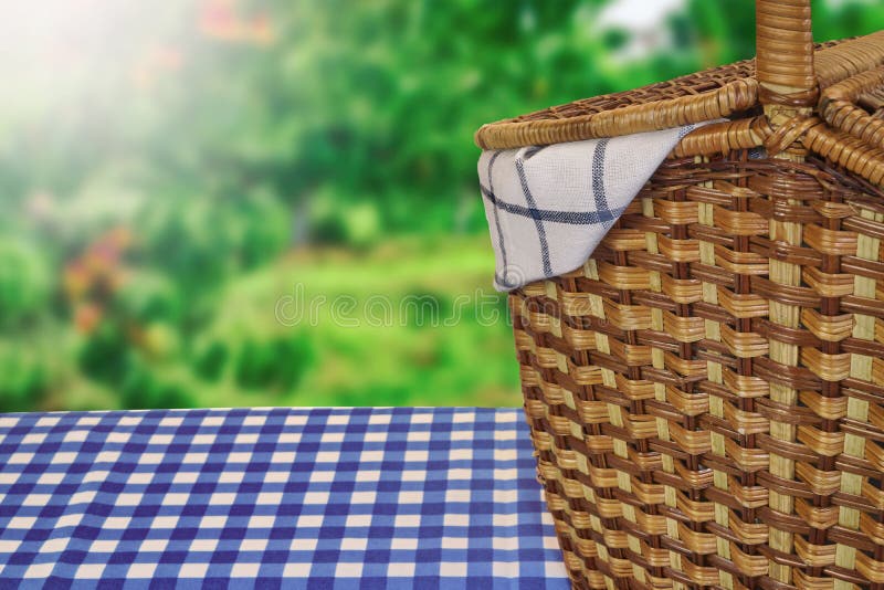 Closeup Of Picnic Basket On The Table With Blue Checkered Tablecloth And Summer Garden In The Background. Closeup Of Picnic Basket On The Table With Blue Checkered Tablecloth And Summer Garden In The Background