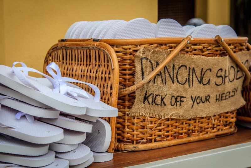 Basket with white flip-flops of different sizes for guests, with a writing DANCING SHOES. KICK OFF YOUR HEELS! Close-up. Basket with white flip-flops of different sizes for guests, with a writing DANCING SHOES. KICK OFF YOUR HEELS! Close-up