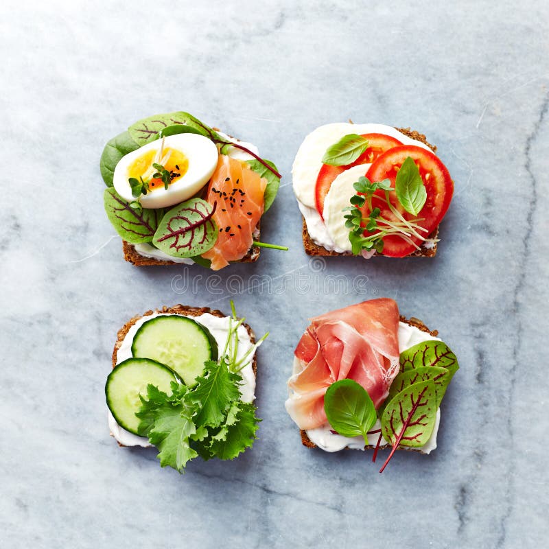 Panini aperti sani con le verdure, il salmone, il prosciutto, le erbe ed il formaggio a pasta molle fotografie stock Panini aperti sani con le verdure, il salmone, il prosciutto, le erbe ed il formaggio a pasta molle fotografie stock