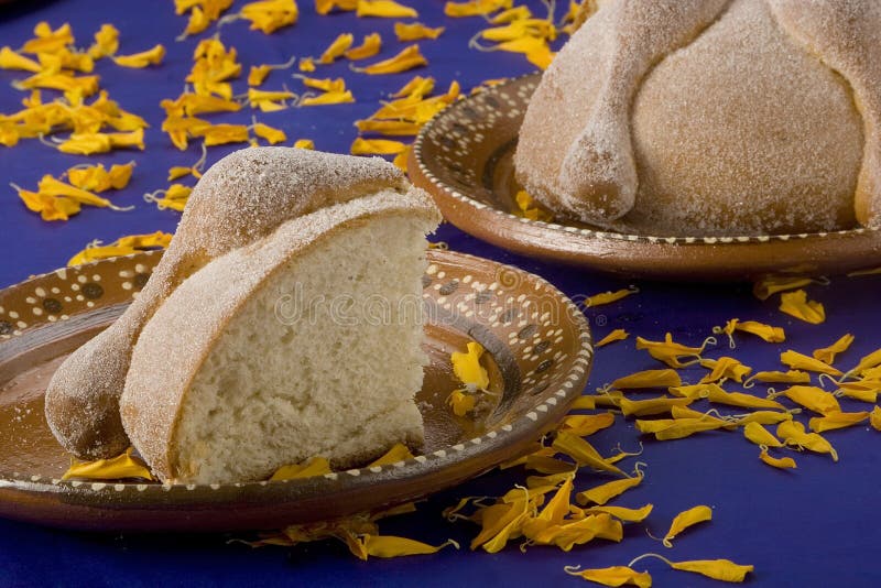 Slice of bread on clay plate made for the celebration on November 2, known as Day of Dead (Dia de muertos). Yellow petals of Cempazuhitl flower over blue background. Slice of bread on clay plate made for the celebration on November 2, known as Day of Dead (Dia de muertos). Yellow petals of Cempazuhitl flower over blue background