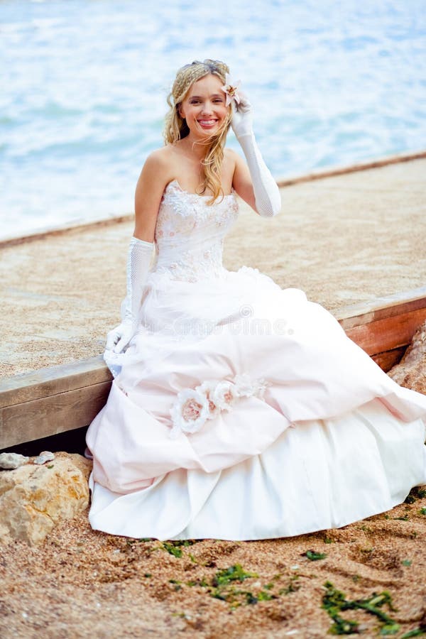 Beautiful happy bride itting on berth at beach and smiling. Beautiful happy bride itting on berth at beach and smiling