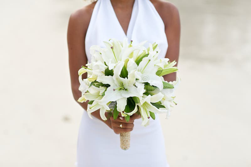 Bride holding white lily flower wedding bouquet on white sand beach. Bride holding white lily flower wedding bouquet on white sand beach