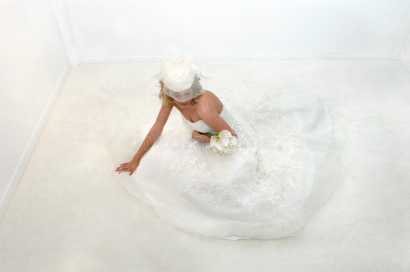 High angle shot shows bride wearing sophisticated hat with white netting. Bride reclining on white carpet. Calilillies lay across her arm. High angle shot shows bride wearing sophisticated hat with white netting. Bride reclining on white carpet. Calilillies lay across her arm.