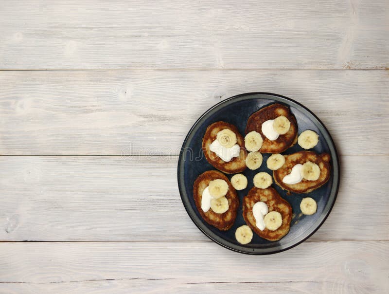 Pannelli di latticello con banane e crema acida in un piatto su uno sfondo di legno leggero Vista in alto, piano piano immagine stock libera da diritti Pannelli di latticello con banane e crema acida in un piatto su uno sfondo di legno leggero Vista in alto, piano piano immagine stock libera da diritti