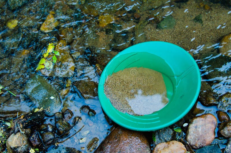 Gold panning goldpan filled with mineral rich soil,  in gold bearing stream.  Fun, recreational outdoor activity of prospecting for gold and gemstones. Gold panning goldpan filled with mineral rich soil,  in gold bearing stream.  Fun, recreational outdoor activity of prospecting for gold and gemstones.