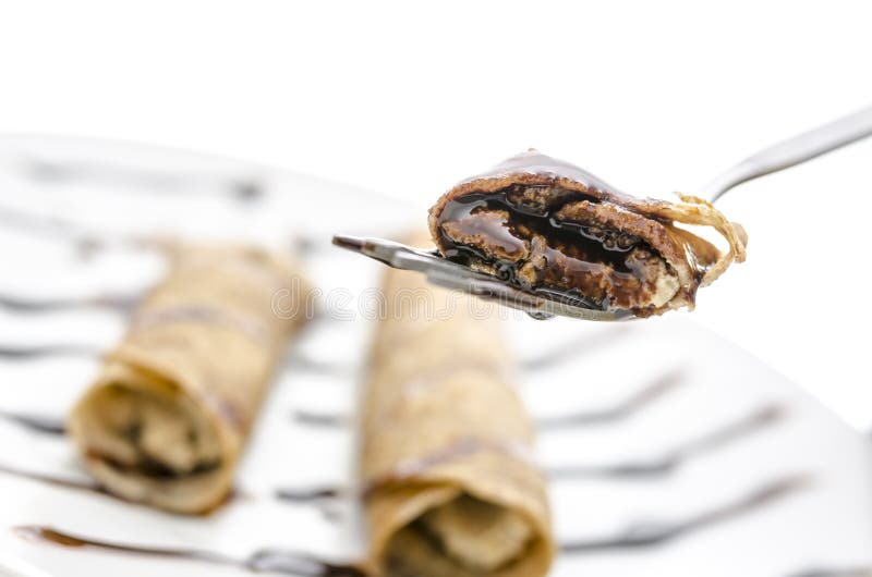 Pancake with liquid chocolate on a fork. With blurred pancakes on a plate in background. Pancake with liquid chocolate on a fork. With blurred pancakes on a plate in background.