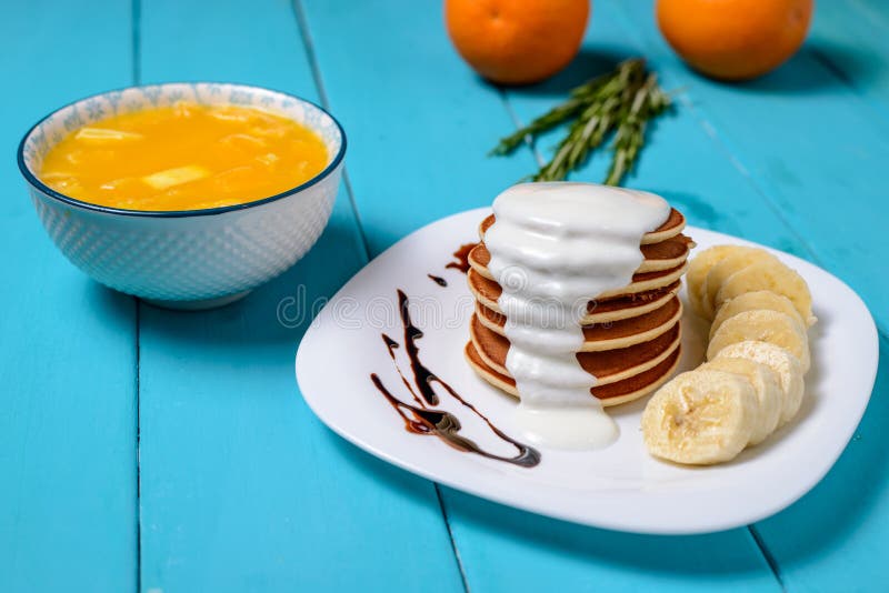Pannkakor med yoghurt- och bananstycken, orange fruktsaft arkivbild Pannkakor med yoghurt- och bananstycken, orange fruktsaft arkivbild