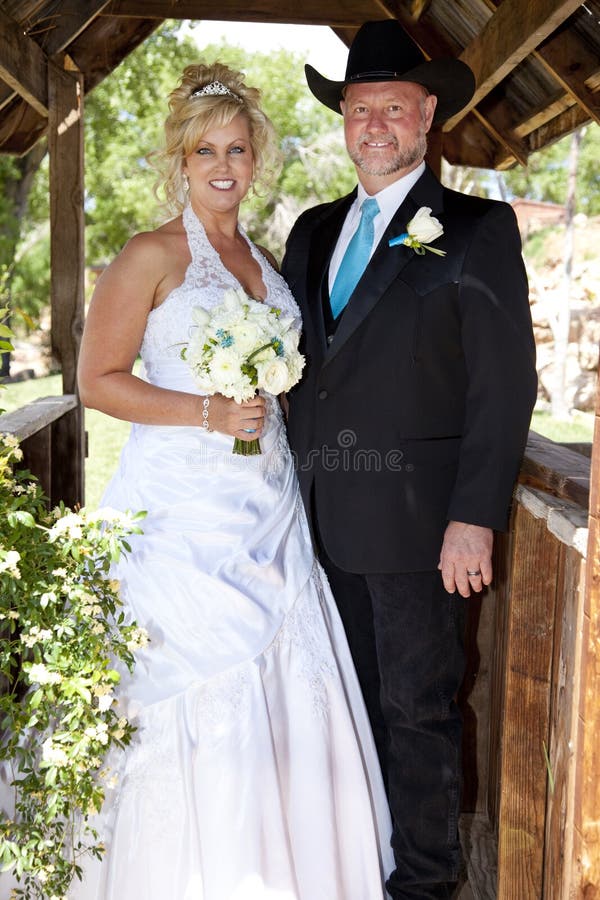 Bride and groom poses outdoors in a lovely wedding gown and a western-style suit with cowboy hat. Bride and groom poses outdoors in a lovely wedding gown and a western-style suit with cowboy hat.