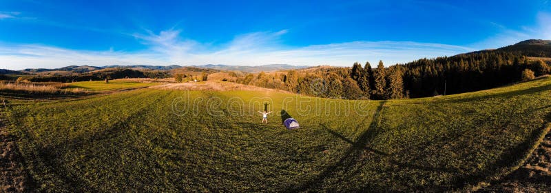 Panorama aerial view of happy hiker woman with open arms stay near tent around mountains sunset horizon enjoying the leisure royalty free stock images Panorama aerial view of happy hiker woman with open arms stay near tent around mountains sunset horizon enjoying the leisure royalty free stock images
