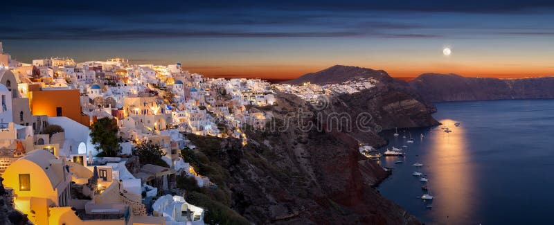 Panorama av byn av Oia på ön av Santorini med fullmånen arkivbild Panorama av byn av Oia på ön av Santorini med fullmånen arkivbild