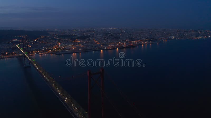 Panorama aéreo nocturno del centro urbano de lisboa en luces con el puente rojo ponte 25 de abril cruzando el mar almacen de metraje de vídeo