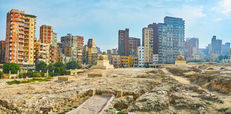 Panorama of Serapeum Temple ruins with two statues of sphinxes and residential high-rises on the distance, Amoud Al Sawari archaeological site, Alexandria, Egypt. Panorama of Serapeum Temple ruins with two statues of sphinxes and residential high-rises on the distance, Amoud Al Sawari archaeological site, Alexandria, Egypt.