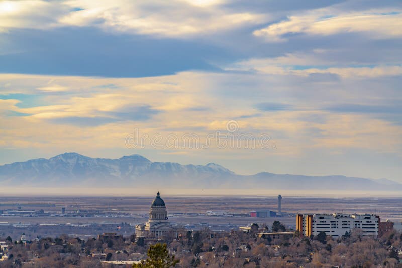 Panorama of downtown Salt Lake City against majestic mountain and cloudy sky. The Utah State Capital Building towers prominently over the cityscape.