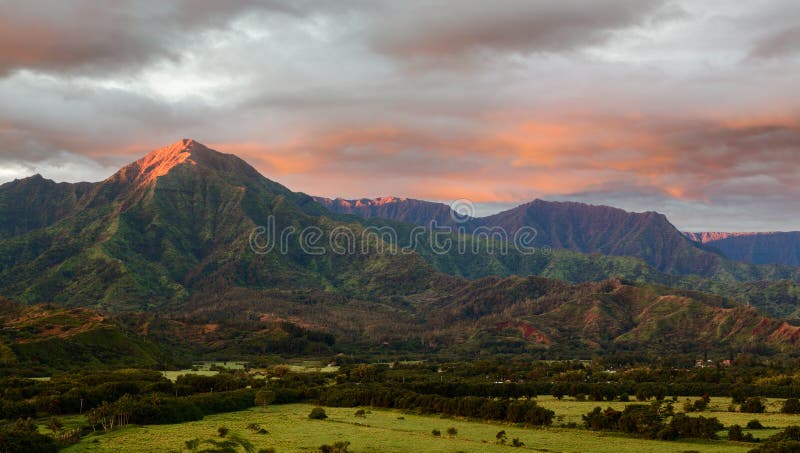 Mountains of the Na Pali mountain range in the distance above Hanalei Bay in Kauai. Taken just after dawn with the sun just skimming the peaks of the mountains and illuminating the clouds with a brilliant red light. Mountains of the Na Pali mountain range in the distance above Hanalei Bay in Kauai. Taken just after dawn with the sun just skimming the peaks of the mountains and illuminating the clouds with a brilliant red light