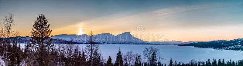 Panorama of late evening sunset in winter Rossvatnet lake Mountains in Northern Sweden - frozen lake with and and bjork in the in