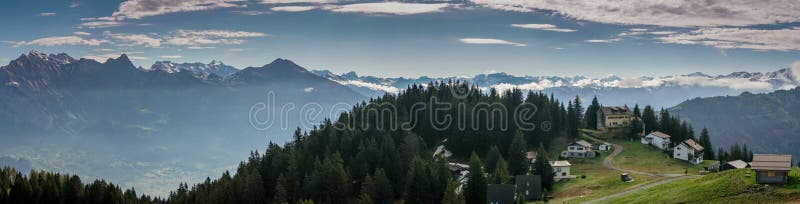 A panorama view of a mountain landscape in the Swiss Alps with huts and chalets in the foreground. A panorama view of a mountain landscape in the Swiss Alps with huts and chalets in the foreground