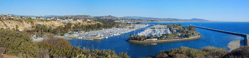 The panoramic image shows the spectacular Dana Point Harbor, Dana Point, California. The construction of Dana Point Harbor started in the late 1960s and dedicated on July, 1971. The marina has 2,500 slips for vessels of various sizes. Part of a protected Coastal Saga biome is seen in the foreground.The image was made from atop the Dana Point Headlands, a 121.3 acre site characterized by scenic and natural features including sheer coastal bluffs, environmentally sensitive habitat areas, scenic vistas, and pedestrian trails. The panoramic image shows the spectacular Dana Point Harbor, Dana Point, California. The construction of Dana Point Harbor started in the late 1960s and dedicated on July, 1971. The marina has 2,500 slips for vessels of various sizes. Part of a protected Coastal Saga biome is seen in the foreground.The image was made from atop the Dana Point Headlands, a 121.3 acre site characterized by scenic and natural features including sheer coastal bluffs, environmentally sensitive habitat areas, scenic vistas, and pedestrian trails.