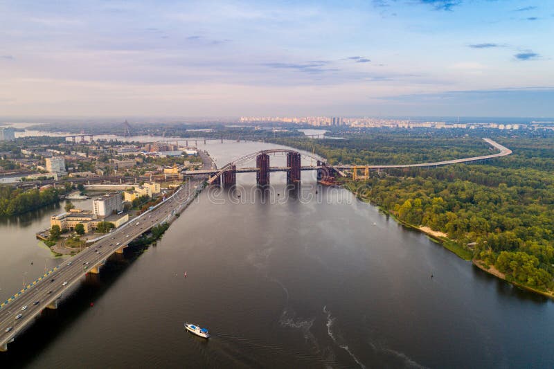 Panoramautsikten av en modern stad med en flod, oavslutad bro och parkerar delen av staden royaltyfri bild Panoramautsikten av en modern stad med en flod, oavslutad bro och parkerar delen av staden royaltyfri bild
