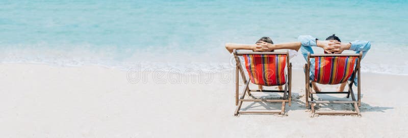 Panoramic banner image of a sweet couple whilst sitting on deck chairs a blue sky on a beach vacation, honeymoon trip. wide crop