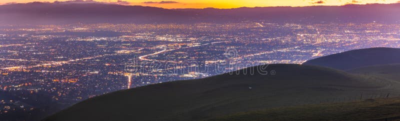 Panoramic night view of San Jose, Silicon Valley; the downtown area buildings visible on the right; green hills partially blocking