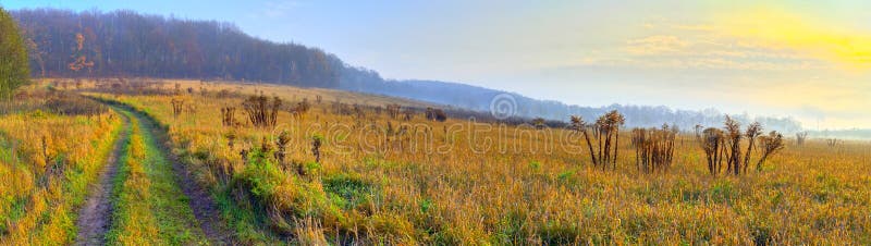 Autumn landscape with rural road, grassy meadows and forest on hill. Panoramic HDR image. Poland, Swietokrzyskie. Autumn landscape with rural road, grassy meadows and forest on hill. Panoramic HDR image. Poland, Swietokrzyskie.