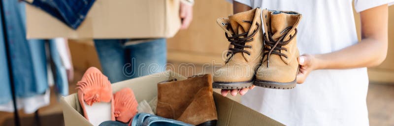 Panoramic shot of african american volunteer holding kids shoes while standing near carton box with footwear. Panoramic shot of african american volunteer stock photos Panoramic shot of african american volunteer holding kids shoes while standing near carton box with footwear. Panoramic shot of african american volunteer stock photos