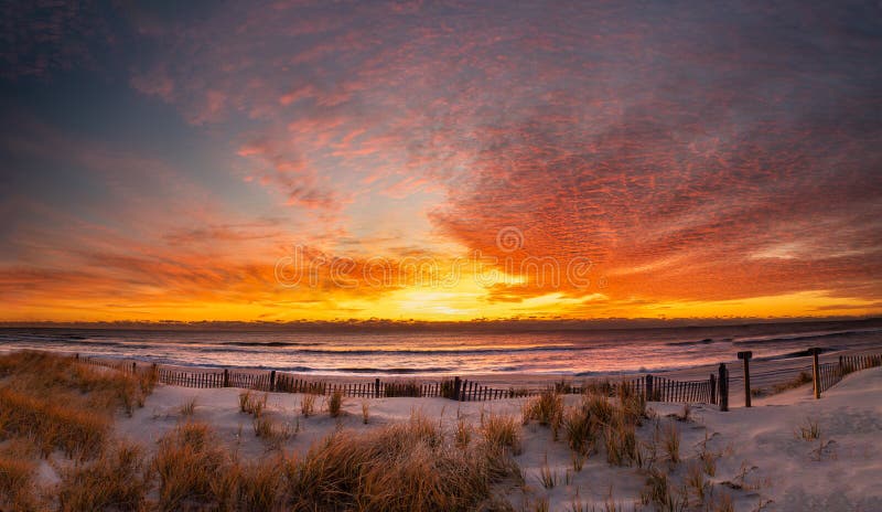 Panoramic sunrise at the beach with a dune fence in the foreground