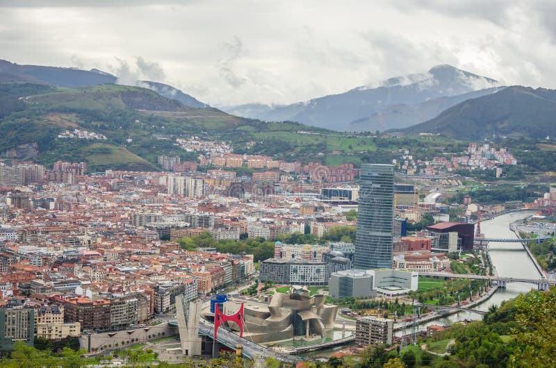 Panoramic aerial view of Bilbao city, showcasing the modern architecture of the Guggenheim Museum, the Nervión River, and surrounding urban landscape from Artxanda hill.