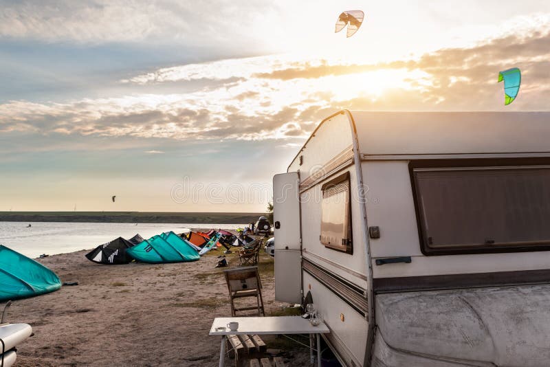 Panoramic view of many surf board kite riders on sand beach watersport spot bright sunny day against old rv camper van