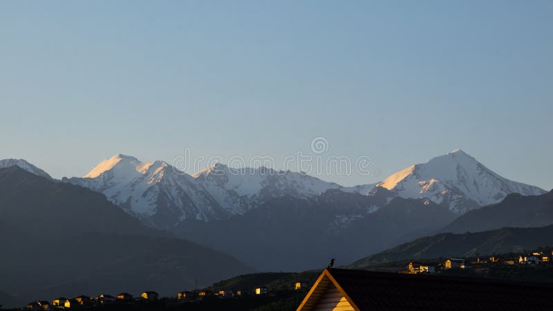Panoramic view of the snow-capped mountains of the Trans-Ili Alatau over the houses during the summer sunrise.
