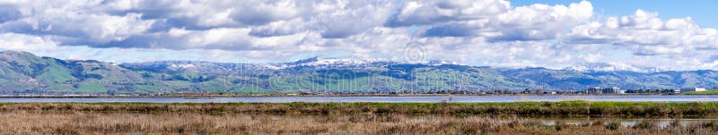 Panoramic view towards green hills and snowy mountains on a cold winter day taken from the shores of a marsh in south San