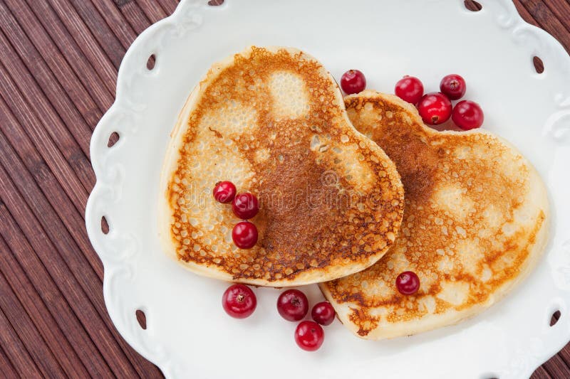 Heart shaped pancakes with cranberries on white porcelain plate. Celebration dessert. Closeup. Heart shaped pancakes with cranberries on white porcelain plate. Celebration dessert. Closeup.