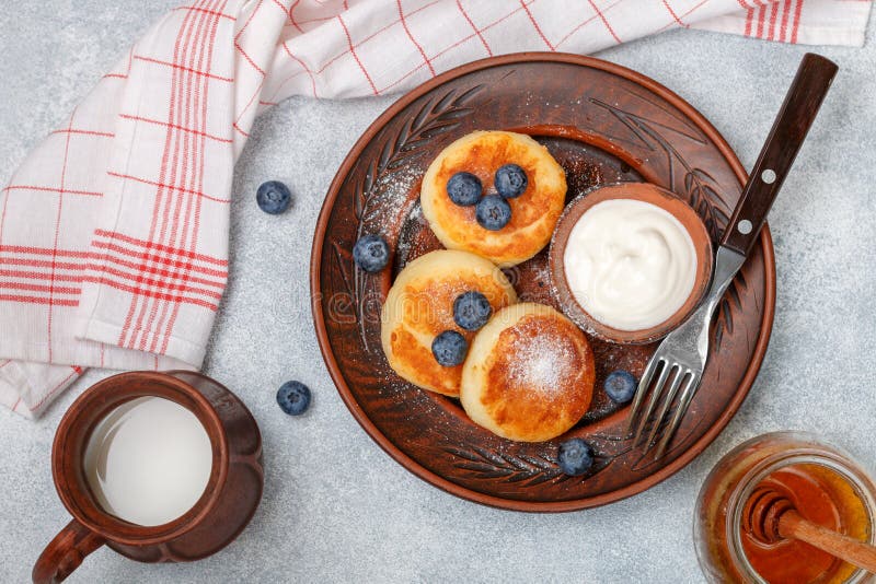 Panquecas do requeijão, syrniki, fritos do coalho com o mirtilo fresco da baga, açúcar pulverizado, leite, mel e creme de leite imagens de stock Panquecas do requeijão, syrniki, fritos do coalho com o mirtilo fresco da baga, açúcar pulverizado, leite, mel e creme de leite imagens de stock