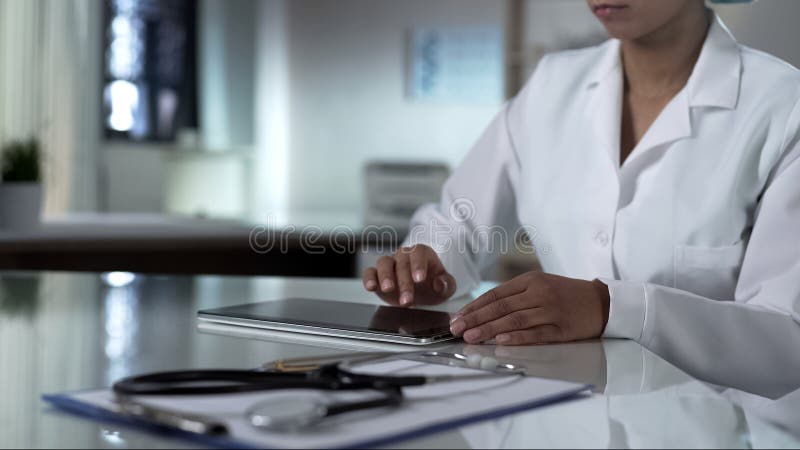 Pantalla femenina de la tableta del movimiento en sentido vertical del doctor, comprobando resultados de la prueba de los pacient imagen de archivo libre de regalías Pantalla femenina de la tableta del movimiento en sentido vertical del doctor, comprobando resultados de la prueba de los pacient imagen de archivo libre de regalías