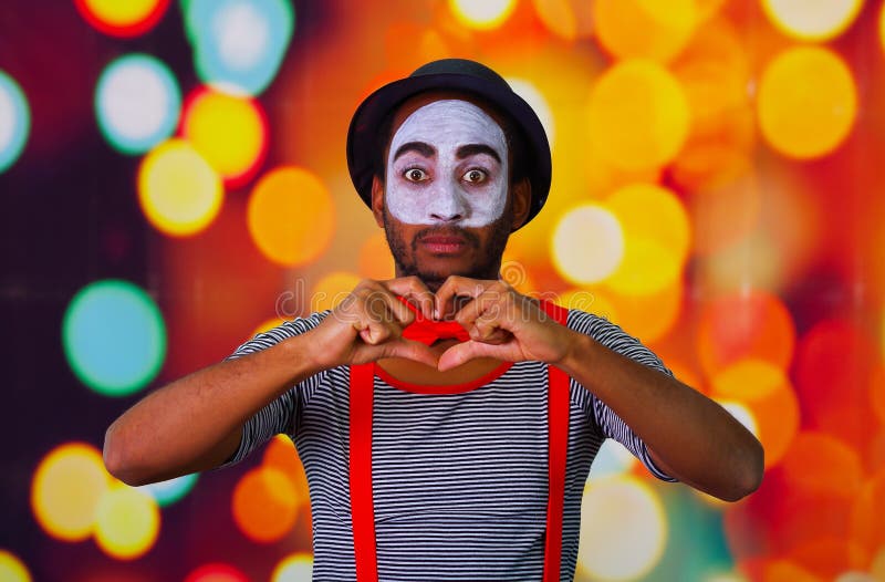 Pantomime man wearing facial paint posing for camera, using hands interacting body language, blurry lights background stock photos