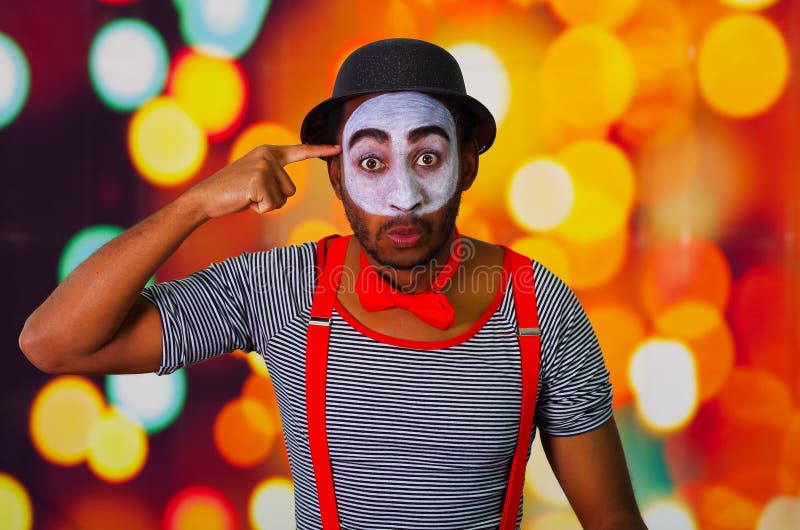 Pantomime man wearing facial paint posing for camera, using hands interacting body language, blurry lights background royalty free stock image