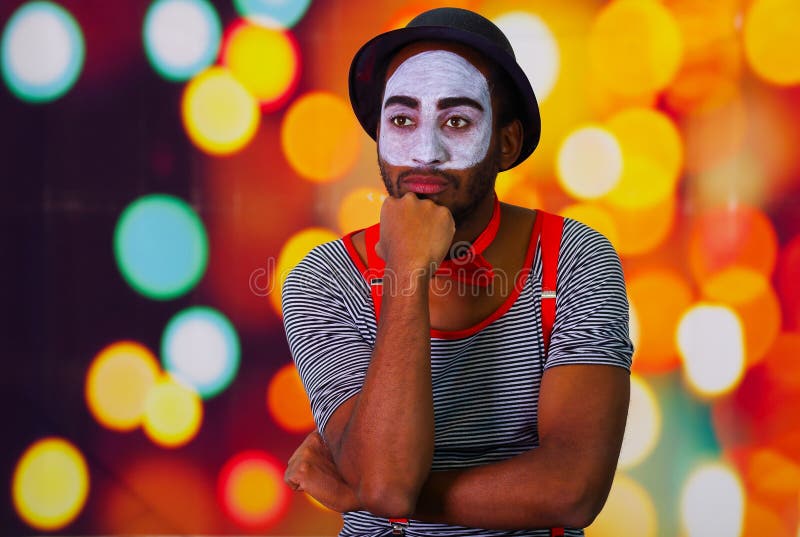 Pantomime man wearing facial paint posing for camera, using hands interacting body language, blurry lights background royalty free stock photos