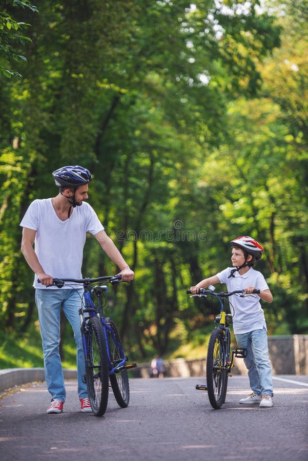 Papa et son fils vélo. Beau jeune père et son mignon petit fils se regardent et sourient en faisant du vélo dans le parc