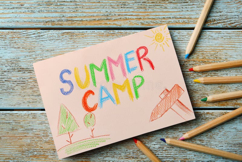 Papel com ACAMPAMENTO DE VERÃO do texto escrito, desenhos e os lápis diferentes no fundo de madeira fotografia de stock Papel com ACAMPAMENTO DE VERÃO do texto escrito, desenhos e os lápis diferentes no fundo de madeira fotografia de stock