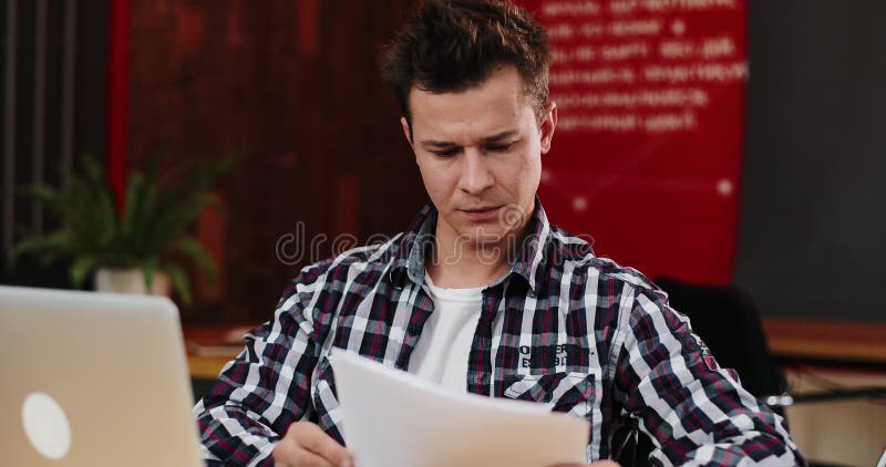 Papeleo joven feliz de la lectura del hombre de negocios en el escritorio en oficina Hombre casual que sonríe en el trabajo Hombr