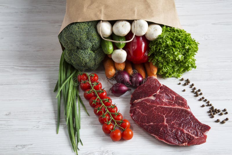 Paper bag of different vegetables and fruits on wooden background. Healthy food.