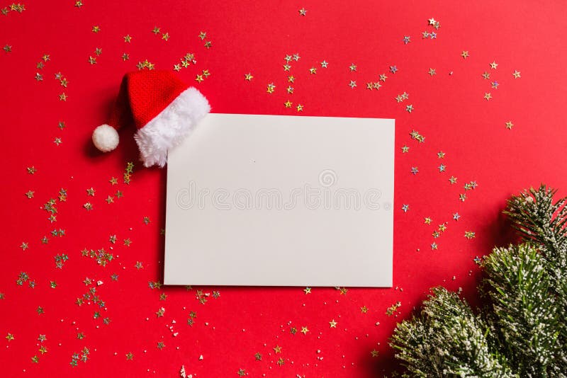 Blank of paper with Santa hat, gift, tree branches on red background with golden confetti. new year concept. Greeting card, xmas. Paper blank, Christmas branches stock image