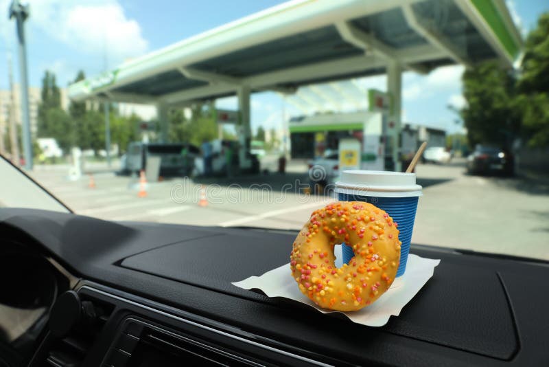 Paper Coffee Cup and Doughnut on Car Dashboard at Gas Station Stock