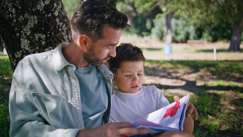 Papi niño leyendo reunión de cuentos de hadas en el closet de los bosques. Hijo del padre hablando imagen de archivo