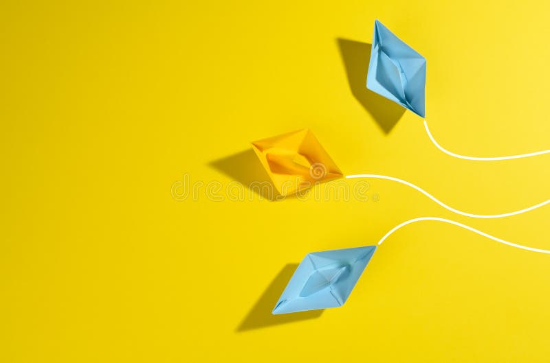 Paper boats sail in different directions on a yellow background. the concept of leadership, achieving goals and disunity, top view. Paper boats sail in different directions on a yellow background. the concept of leadership, achieving goals and disunity, top view