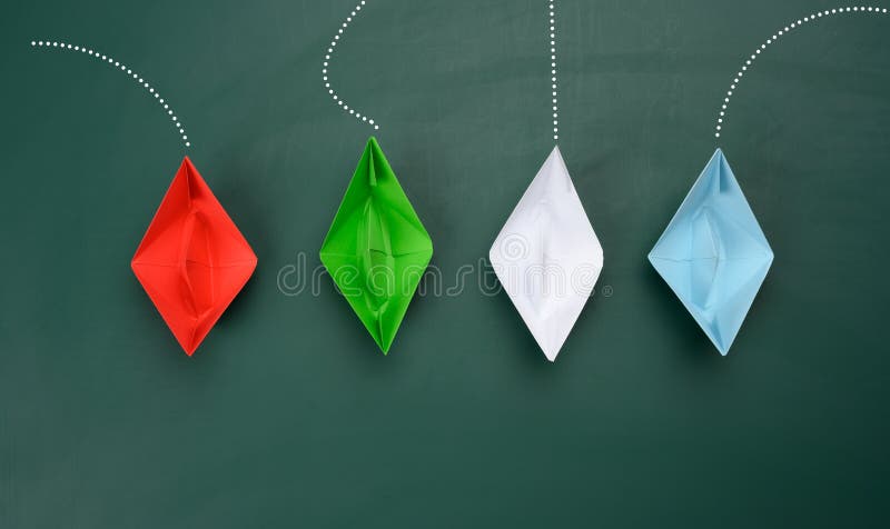 Paper boats sail in different directions on a green background. concept of leadership, achieving goals and disunity, top view. Paper boats sail in different directions on a green background. concept of leadership, achieving goals and disunity, top view