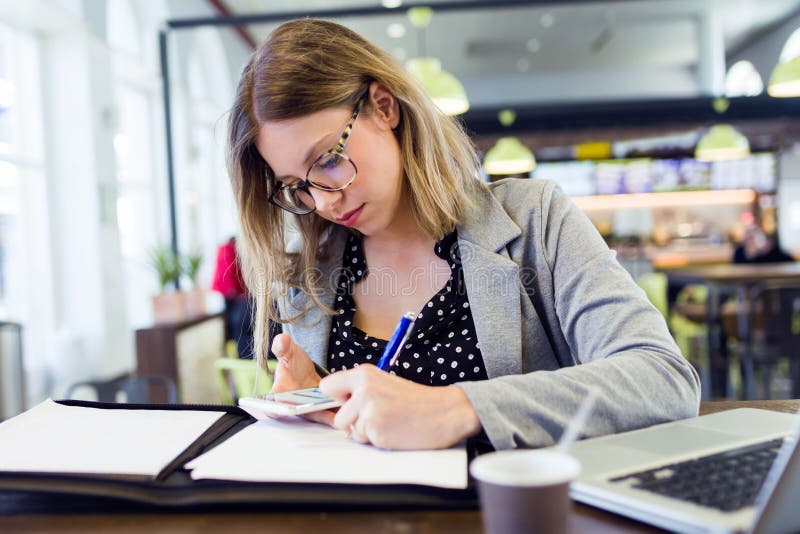 Papiers à lettres assez jeunes de femme d'affaires tout en à l'aide de son téléphone portable en café photo stock Papiers à lettres assez jeunes de femme d'affaires tout en à l'aide de son téléphone portable en café photo stock